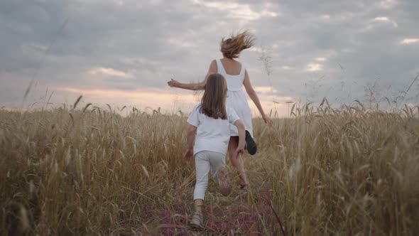 Daughter and Mother Dream Together Run in the Wheat Field at Sunset