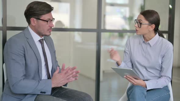 Serious Young Female with Tablet Talking with Middle Aged Businessman