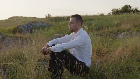 Serious Bearded Man in White Shirt Sits on Green Plant