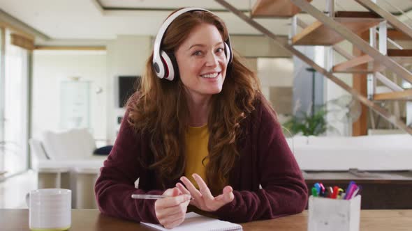 Caucasian woman sitting at desk wearing headphones having video call smiling