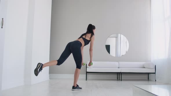 Young Beautiful Brunette Woman Standing on One Leg Doing Bends with Dumbbells. Performing Deadlift