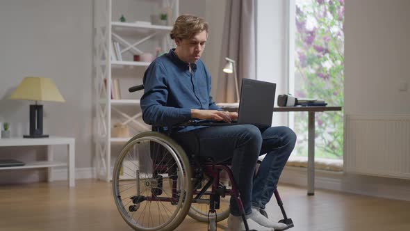 Focused Smart Man in Wheelchair Texting Messaging Online Typing on Laptop Keyboard Thinking