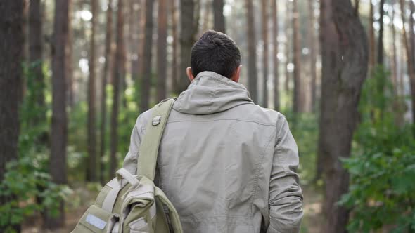 Tracking Shot of Confident Male Adventurer with Backpack Walking in Slow Motion in Forest Turning