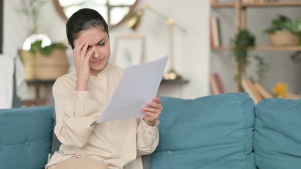 Indian Woman with Documents Reacting To Loss on Sofa 