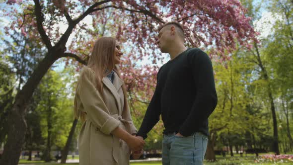 A Beautiful Young Girl is Talking to Her Man and Holding His Hand While Standing Under a Flowering