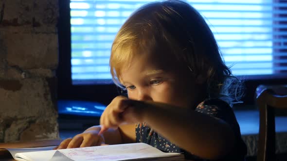 Baby Is Painting In The Album With Lamp Light. Child Is Painting In The Album.