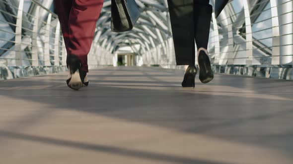 Legs Of Business Women Walking Along Glass Bridge