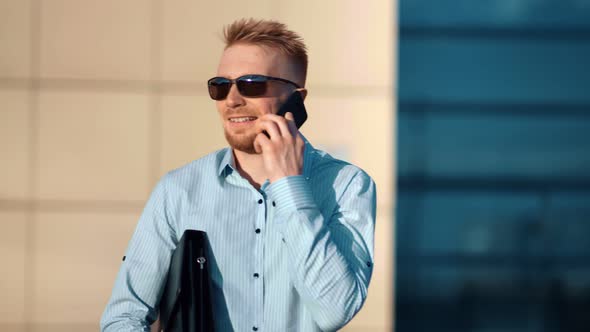 Cheerful Laughing Male Businessman Enjoying Discussing Using Mobile Phone at Building Background