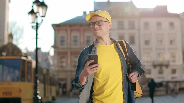 Portrait of a Happy Young Delivery Man Who is Going and Texting on the Smartphone