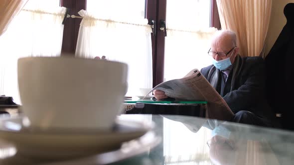 A Grayhaired Man with Glasses and a Black Jacket Reads a Fresh Newspaper While Reading in a Cafe