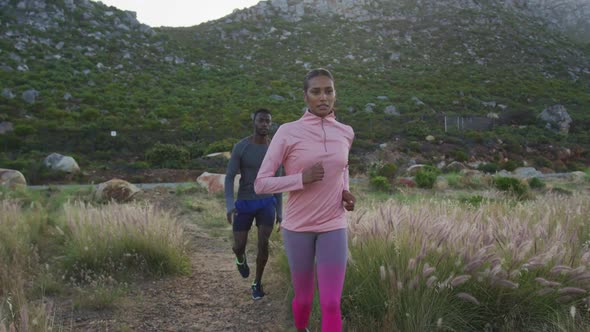 Diverse fit couple exercising running across a field in the countryside