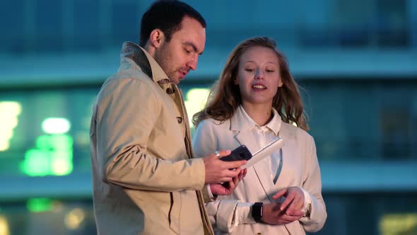 Two Young Work Colleagues Using a Digital Tablet While Standing Together Outside Late at Night