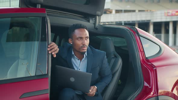 Man with Laptop Sitting Inside Charging Electric Car