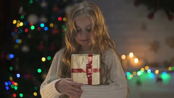 Girl Hugging Present Near Glowing X-Mas Tree and Smiling, Winter Fairy-Tale