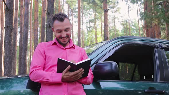 Happy Businessman Crouching on the Hood Smiles and Makes Notes in a Notebook