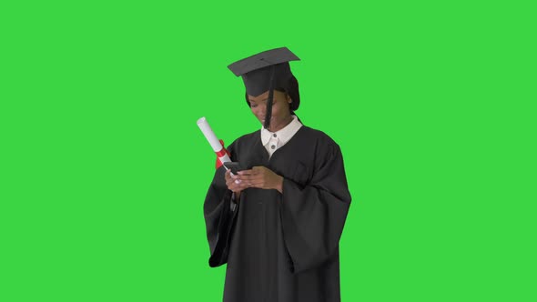 Happy African American Female Graduate Holding Diploma and Texting on Her Phone on a Green Screen