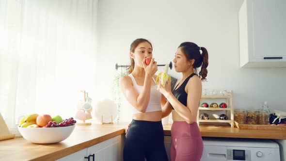 Asian active two women sibling in sportswear eat an apple in kitchen.