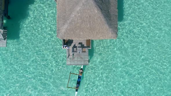 Aerial drone view of a man and woman couple in an overwater bungalow on Bora Bora tropical island.