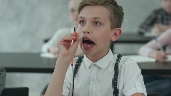 Little Boy Sitting at Table and Listening in Class