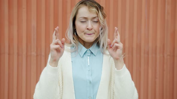 Portrait of Girl Crossing Fingers Making Praying Hands Gesture Standing Alone on Wall Background