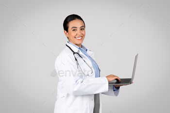 Happy latin woman doctor engaged with laptop on studio background