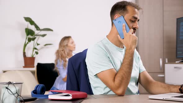 Man Talks on the Phone and Types on the Computer While His Girlfriend Is Playing a Video Game in the