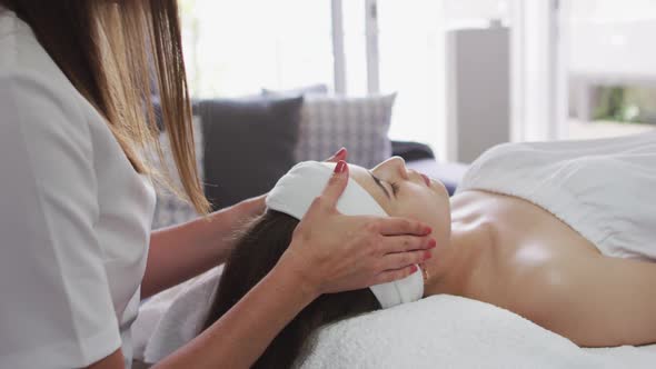 Caucasian woman lying back while beautician gives her a facial