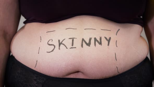 Close-up of Female Caucasian Tummy with Skinny Word Written. Belly of Obese Young Woman. Overweight