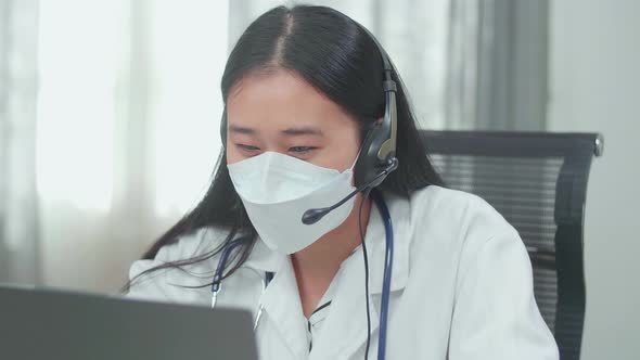 Asian Woman Doctor With Colleague In Masks Working As Call Centre Agent Speaking To Customer