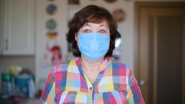 An aged woman in a protective medical mask is looking into the frame