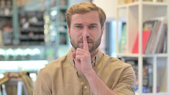 Portrait of Young Man with Finger on Lips Silence Sign