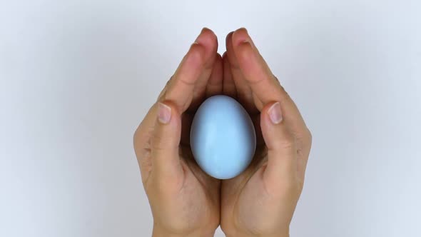 Woman holds a blue egg in her hands and covers it with the palm of her hand.