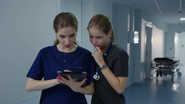 Two Female Nurses are Standing in the Hospital Corridor with a Tablet