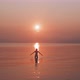 Silhouette of a young woman standing in a calm sea raising her arms in front of the sunrise - VideoHive Item for Sale