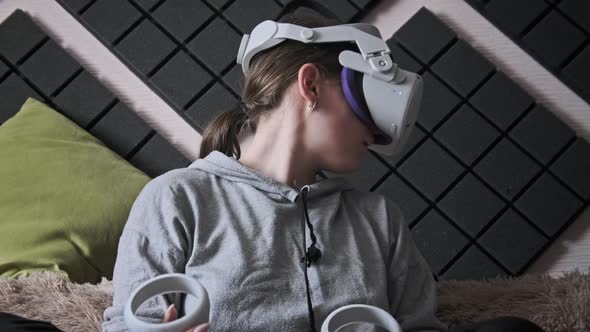 Young Woman Sitting on Sofa Playing Game Using VR Helmet Indoor at Home