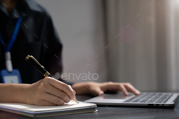 Female hand working search page on computer and writing on a notepad with a pen in the office.