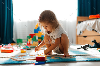 Baby girl playing indoors sitting on floor in playroom at home with constructor. Educational game