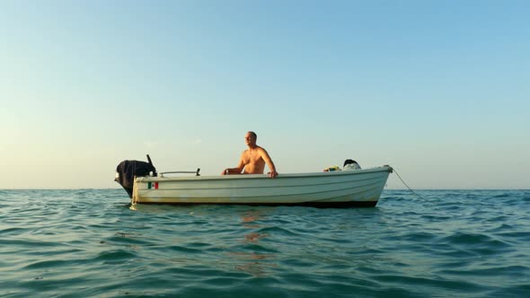 Solitary shirtless man on board of small floating anchored rolling motorboat. Slow-motion low-angle