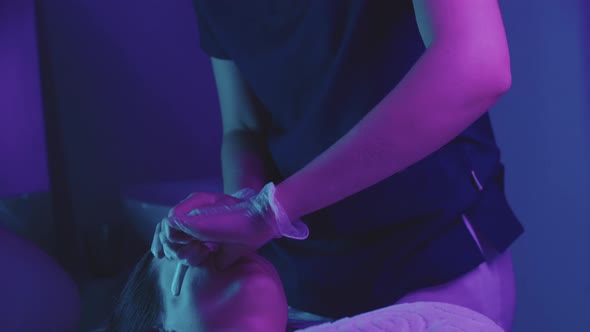 Blonde Young Woman Massagist Doing a Face Massage Using Her Fingers on Her Female Client Neon