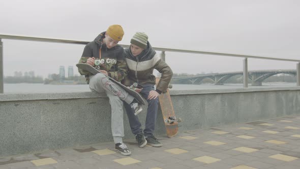 Teen Boys Checking Wheel Mounting on Skate Outdoor