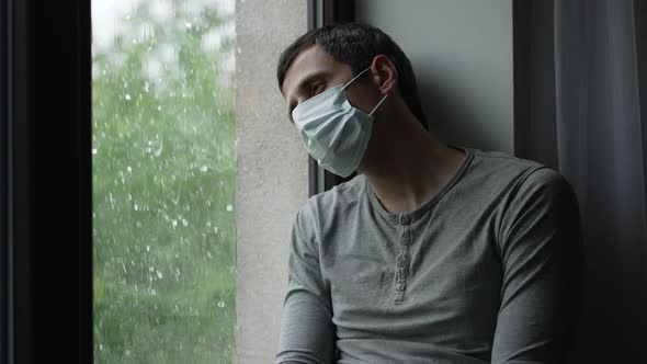 Depressed Man in Mask on Quarantine Looks at the Rain