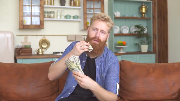 Bearded ginger man eating his money sitting on couch at home.