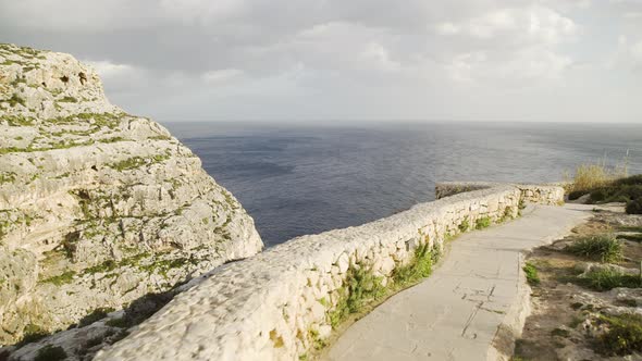 Scenic seaside stone footpath and rock wall with picturesque view of mountain face and blue ocean se