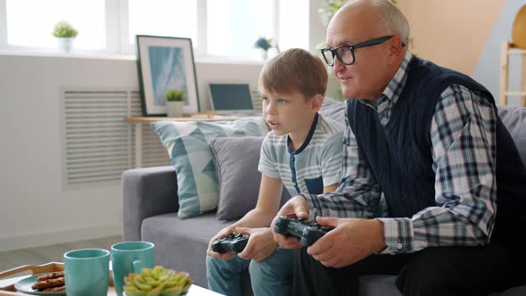 Old Man Playing Video Game with Happy Child Grandson Having Fun at Home alt