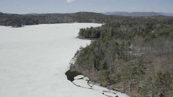 Drone shot flying forwards over a frozen lake with trees on the shores.