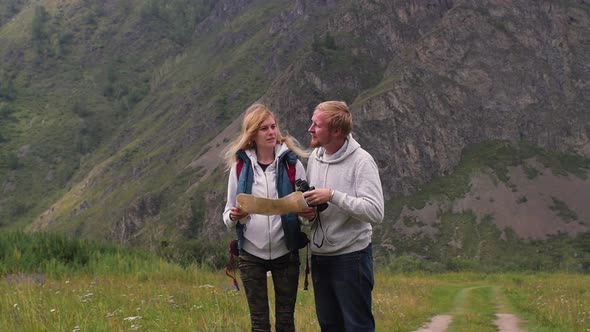 Couple in Love Travels in the Mountains with a Map and Binoculars. Friends Travelers Are Looking for