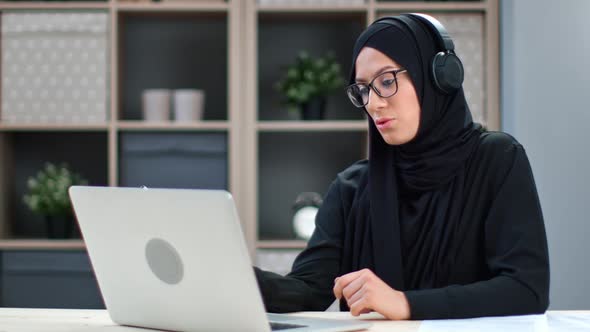 Modern Asian Woman in Black Hijab Wearing Headphones Talking Online Video Call Use Laptop