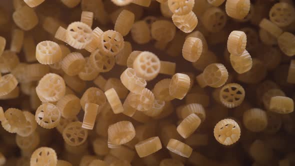 Raw wagon wheels pasta flies after being exploded. Slow Motion.