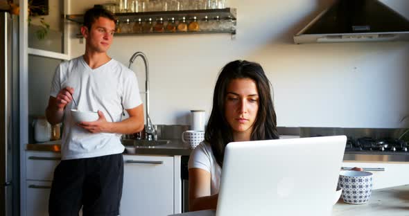 Woman using laptop while man drinking coffee in kitchen