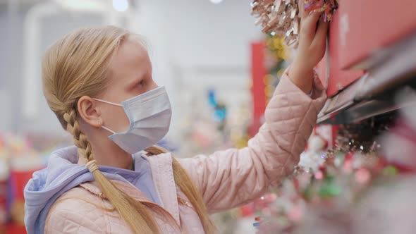 A Child in a Protective Mask Chooses Christmas Tree Toys in the Store